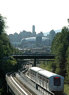 a two car train follows rail tracks under and bridge in the background can