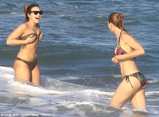 protecting her modesty demi clutches at her bikini top after she and her friend get