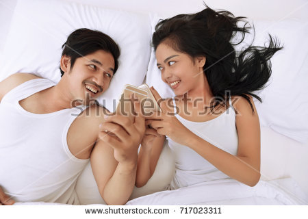 stock photo young asian couple lying down in bed and using mobile phones at home