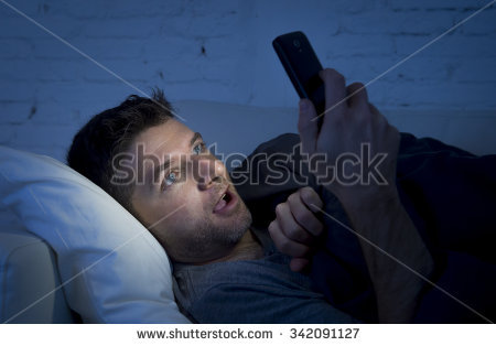 stock photo young man in bed couch at home late at night with intense face expression using mobile phone in low