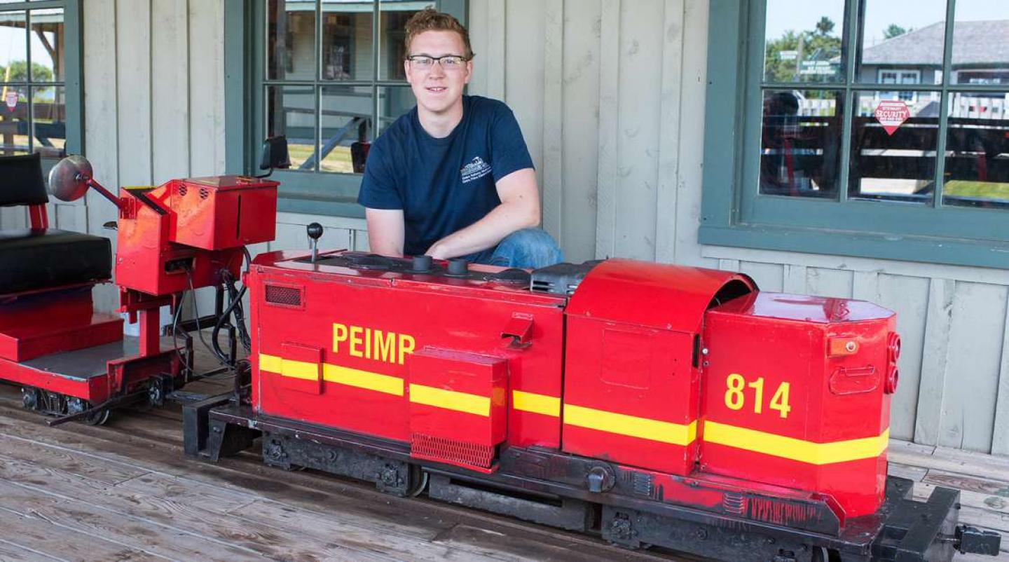 summer student kneels behind mini train at elmira railway museum