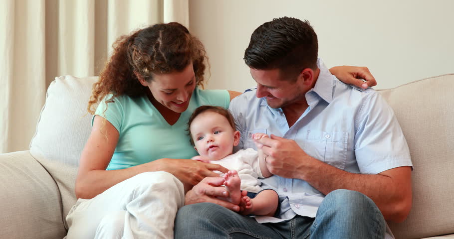 young parents sitting on the couch with their baby son at home in the living room